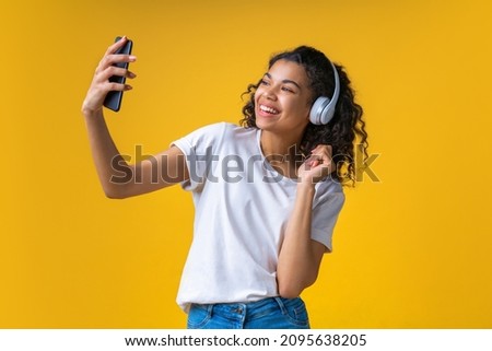 Studio portrait of happy smiling beautful brunette girl wearing wireless headphones and taking selfie on her mobile phone, isolated over yellow background. Photo stock © 