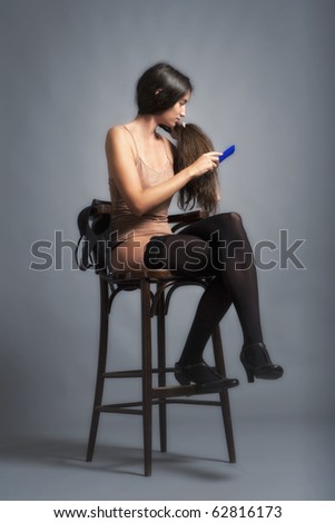 woman sitting on a chair combing her long hair - isolated on gray