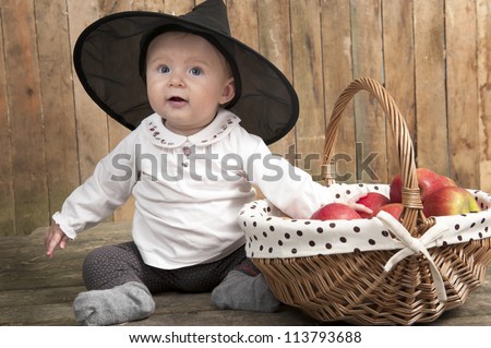 halloween baby with basket of apples, seated on an old wooden floor