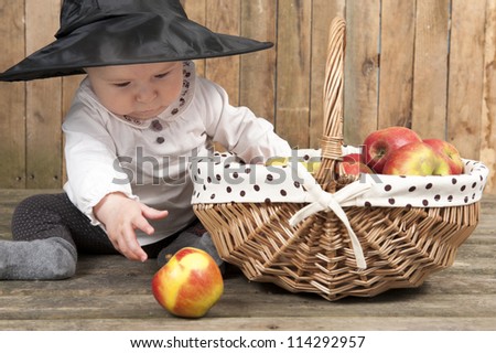 halloween baby with basket of apples, seated on an old wooden floor