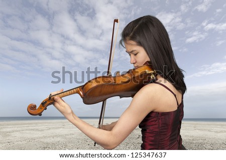 young female violin player outdoors at the beach