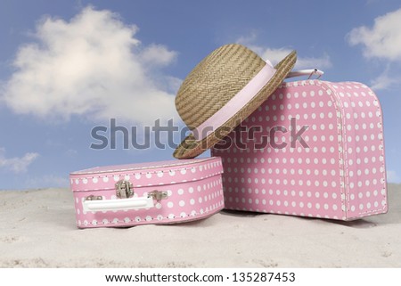 vintage pink with white dots suitcase and straw summer hat at the beach