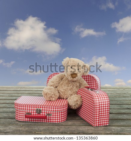 three vintage red and white suitcases with teddy bear ,sky with clouds in background