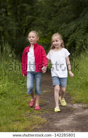 Two Little girls walking hand in hand on a path in the woods
