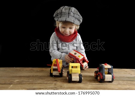 little toddler playing with wooden cars, on black background
