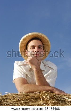 Young man with straw hat on a straw bale looking at the camera