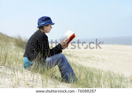 beautiful young woman with book sitting in the dunes at the beach