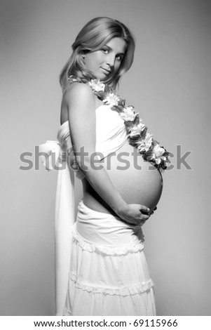 black white pregnant young woman holding her belly with flowers on her neck