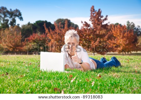 Smiling girl using laptop outdoors and shows well done