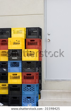 Multiple colored stacked crates beside the back door of a retail building.