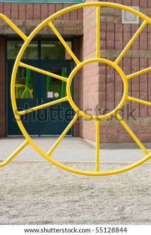 A weird piece of yellow playground equipment with school doors behind.