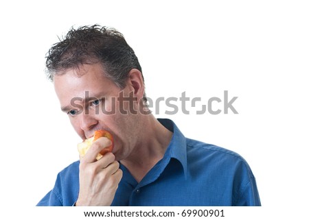A man in a blue dress shirt, eating an apple, isolated on white.