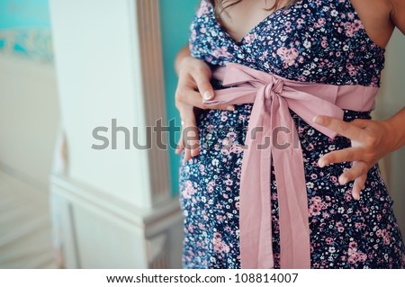 the stomach of the pregnant woman in a color dress and hands holds a tape