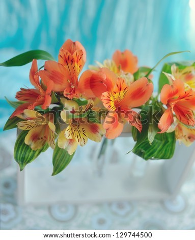 on the window sill with a blue curtain orange spring flowers in a vase