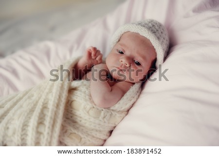 little baby wrapped in a knitted blanket and a white knitted cap