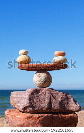 Symbolic scales of stones against the background of the sea and blue sky. Concept of harmony and balance. Pros and cons concept