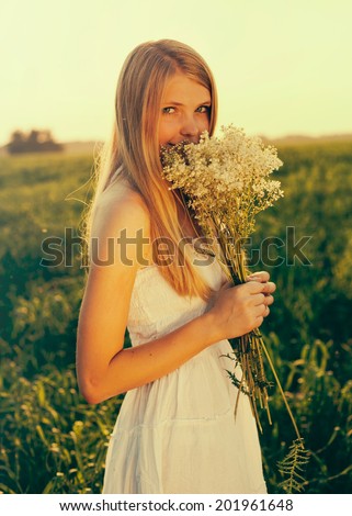 Retro toned portrait of blonde teenage girl with bouquet of wildflowers in summer field