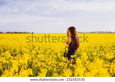 Rear view of young woman with long hair hugging herself on yellow blooming rapeseed field