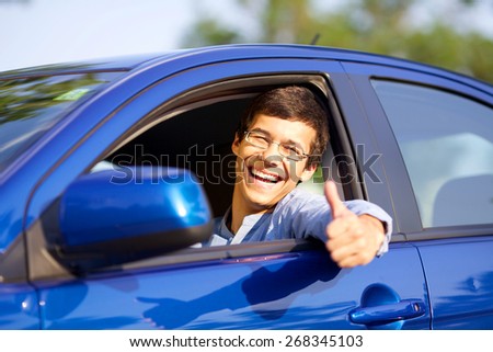 Smiling handsome young driver showing thumb up through open car window