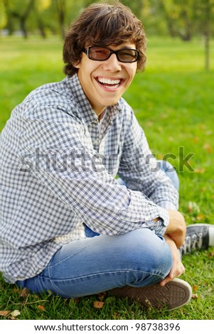Happy college student in black glasses sitting on grass in park at sunny day