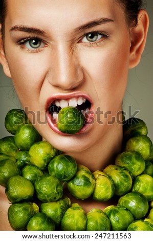 Beautiful woman with fresh Brussels sprouts. Professional makeup. Luxurious green necklace.