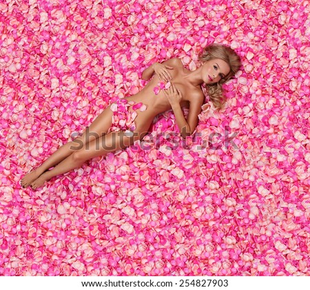 Beautiful slim young woman lying on petals of pink roses. Perfect figure.