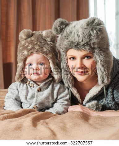 Mother and baby playing and smiling. Happy family.Home interior. Winter season. Fur hats.