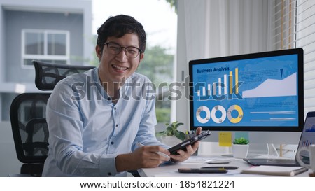 Portrait head shot of young attractive asian man sitting smiling work multiple screen computer and smart tablet on table desk at home in concept freelance data analyst, data scientist for business.