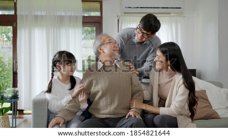 Asian elderly senior male grandpa sitting at sofa couch at home living room on quarantine in concept healthcare, chronic health issue or low back pain in retired older people with family.