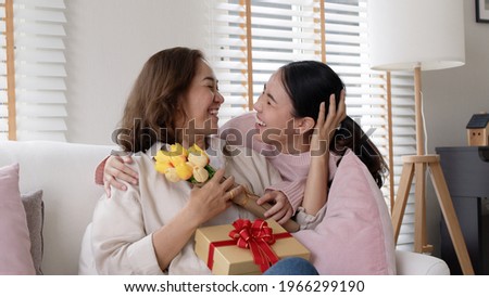 Attractive beautiful asian middle age mum sit with grown up daughter give gift box and flower in family moment celebrate mother day. Overjoy bonding cheerful kid embrace relationship with retired mom. Stock foto © 