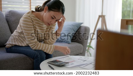 Upset tired young asia woman sit on sofa at home think hard worry in tax expense saving issue past due loan late payment on covid impact life.