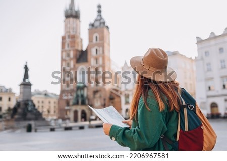 Attractive young female tourist is exploring new city. Redhead girl holding a paper map on Market Square in Krakow. Traveling Europe in autumn. St. Marys Basilica Foto stock © 