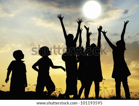 Children rising arms to sun on meadow