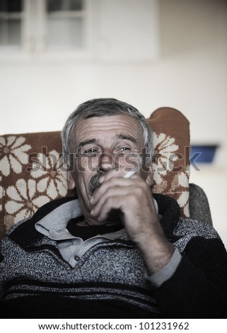 Old man with mustache smoking cigarette while sitting in sofa