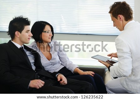 Portrait of modern couple talking to manager while discussing conditions of mortgage using tablet