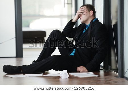 Portrait of a stressed disappointed businessman sitting alone on floor in office