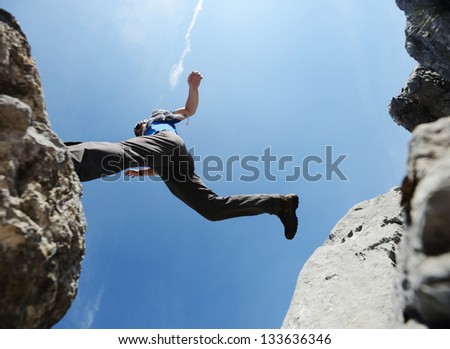 Hiking man jumping over the mountains to success