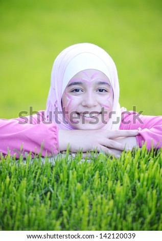 Beautiful teenage Arabic girl lying on green grass in nature