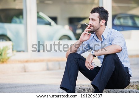 Well dressed man smoking sitting on a street sidewalk