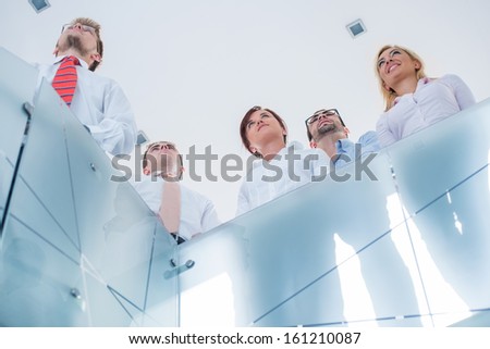 Five happy executive people looking up behind a glass railing