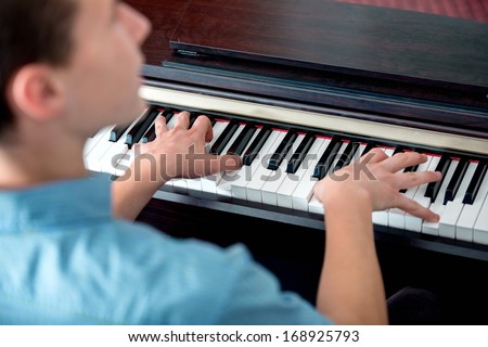 Closeup of young man playing piano from behind