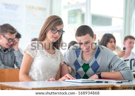 Two teenage students reading together in classroom