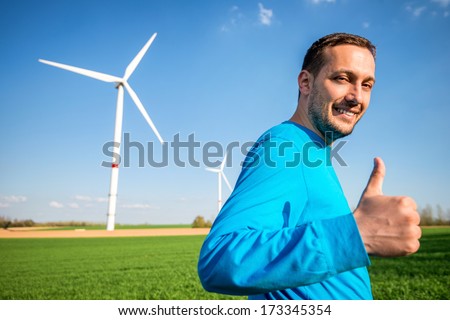 Man standing in wind turbine field with thumb up