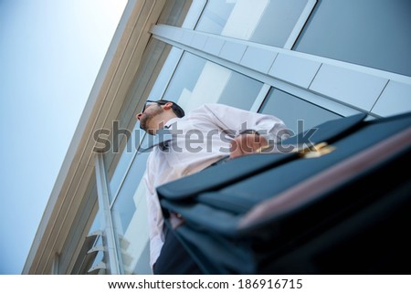Executive man with briefcase in front of modern building shot from below