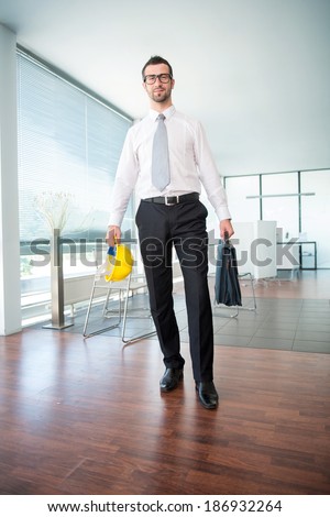 Business man standing with briefcase and hard hat in corporate environment
