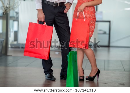 Lower section of two people in formal clothes with paper shopping bags