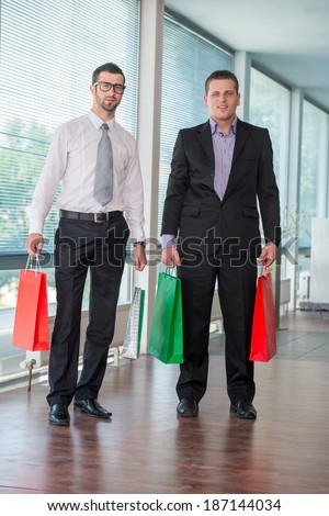 Two business men holding paper bags in modern office posing