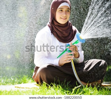 Beautiful Middle Eastern Arabic girl having happy time in summer garden with water sprinkler
