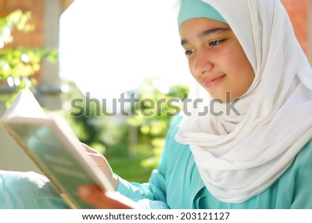 Beautiful Muslim girl reading book with hijab and smiling