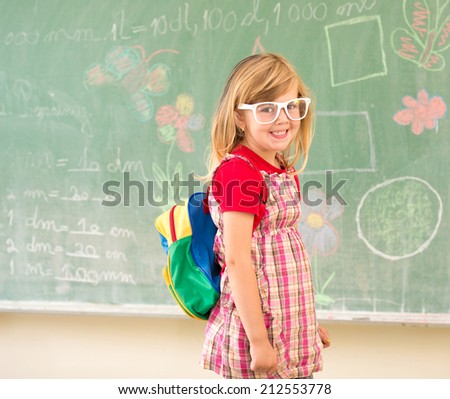 Adorable little school blonde girl in school classroom on board posing